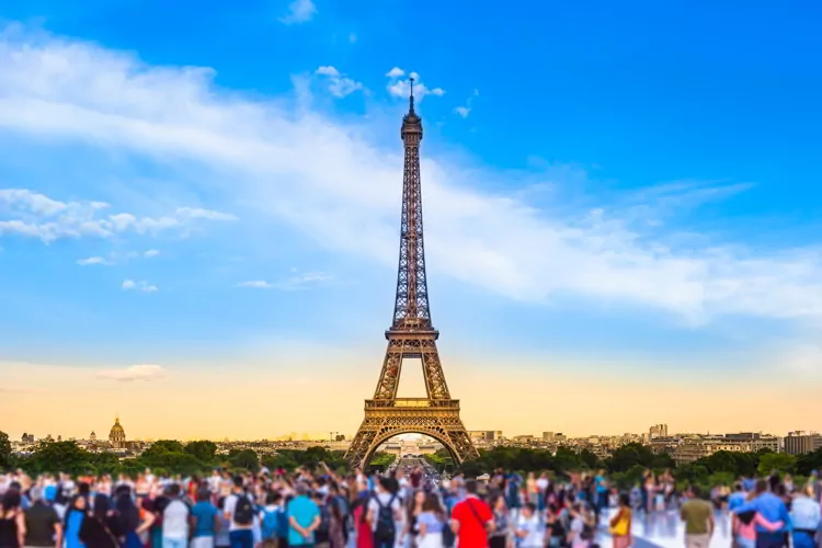 Colorful large group of unrecognizable people blurred in front of Paris Eiffel Tower at evening