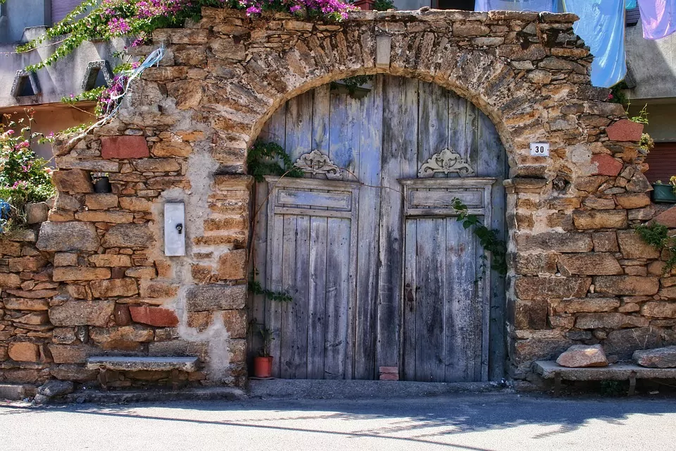 Image of an old gate in sardinia. the gate is wooden and the wall and ark in old stone