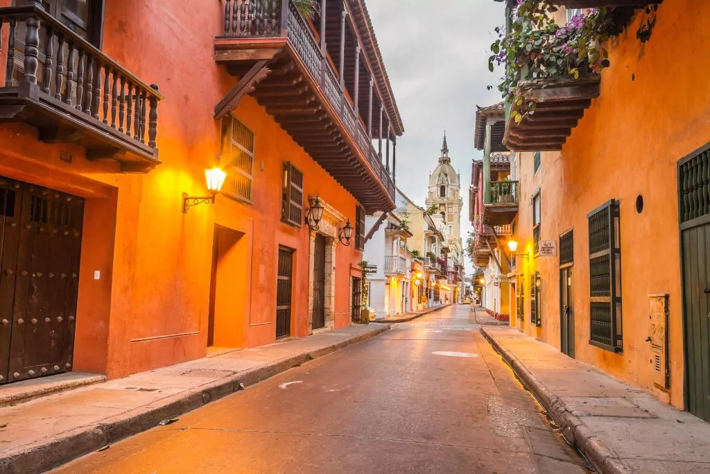 Image of a street in the walled city of cartagena, colombia. Orange houses line a wide open road with a church spire in the background