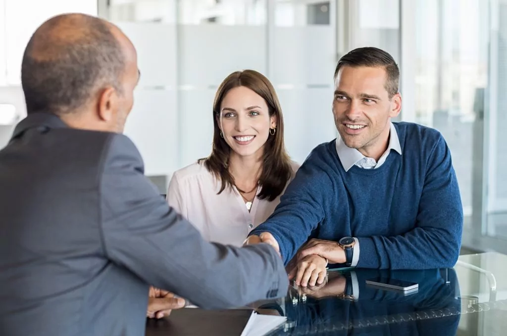 Businessman shaking hand with a young couple in office. Bank agent and his client shaking hands in conference room. Happy smiling couple seal a deal with their personal financial advisor.