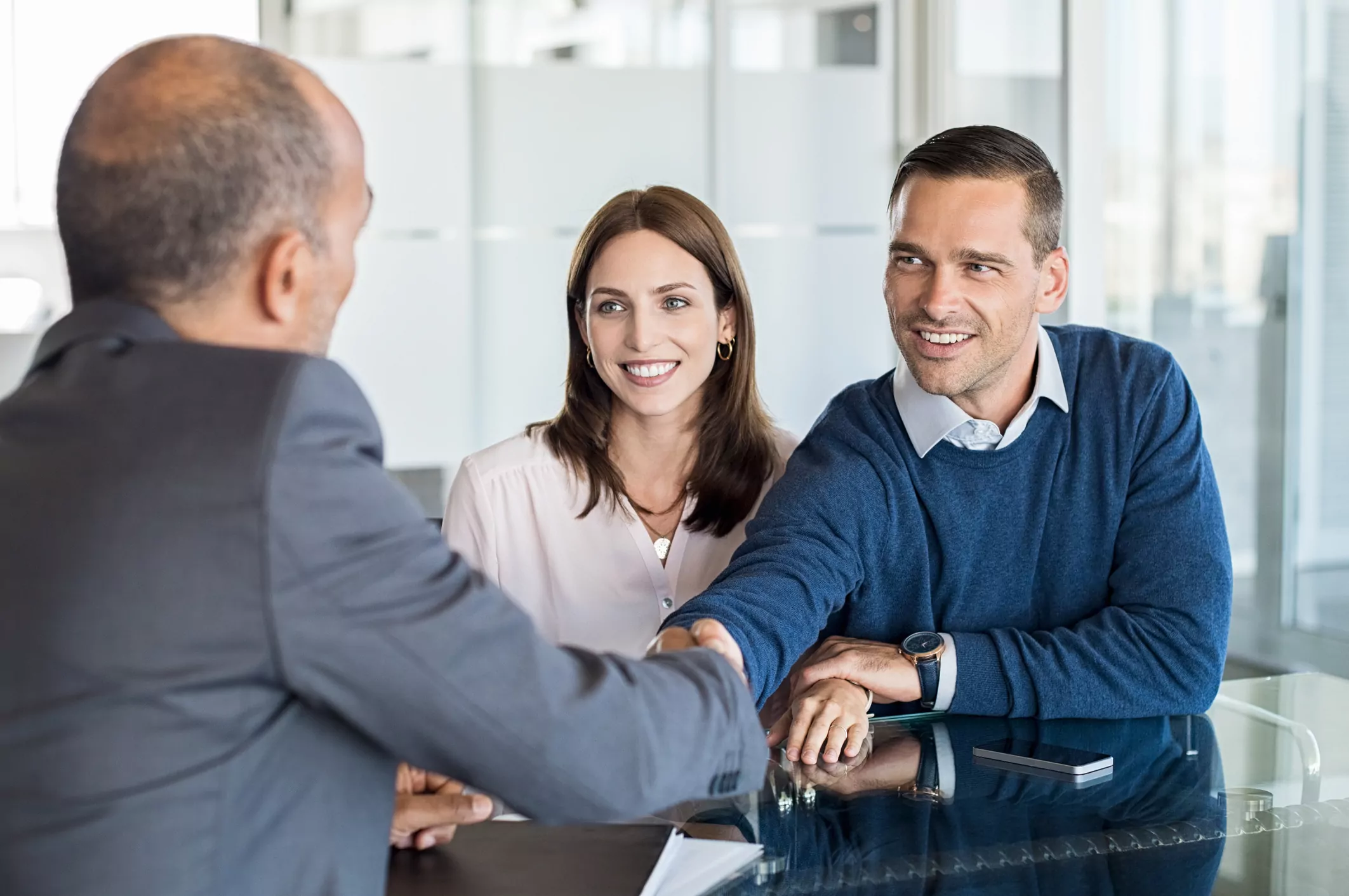 Businessman shaking hand with a young couple in office. Bank agent and his client shaking hands in conference room. Happy smiling couple seal a deal with their personal financial advisor.
