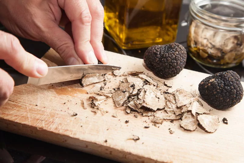 Black truffles being cut by a knife on a chopping board