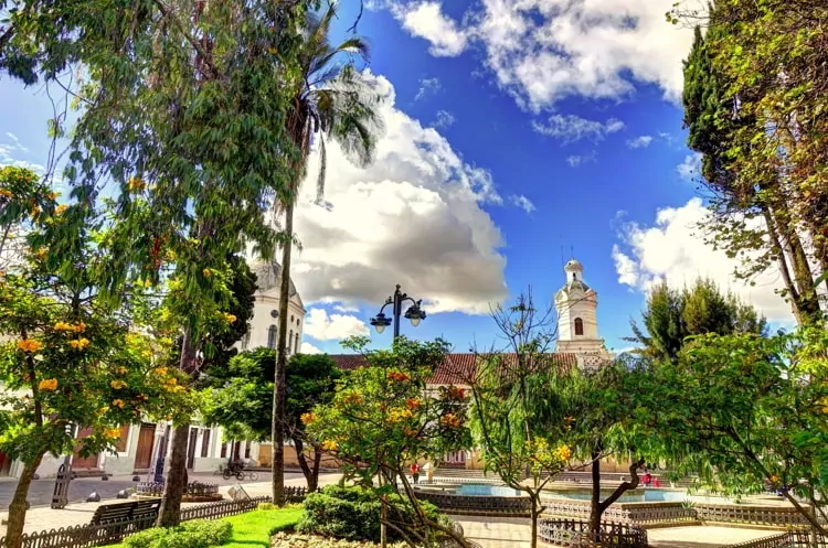 Sunny day in Cuenca, Ecuador. Green trees with a white church on the background.