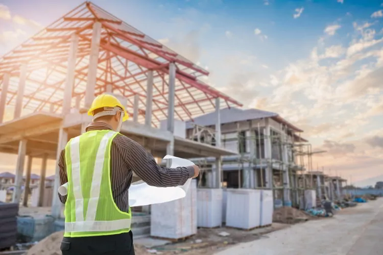 Engineer with protective helmet and blueprints paper at house building construction site