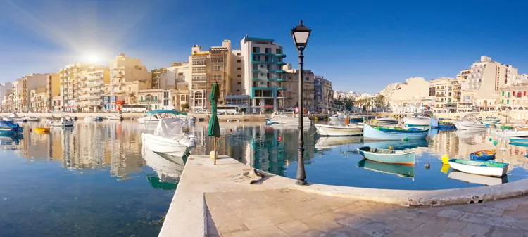 Boats in blue waters in Malta with residential buildings on the backgrounds on a sunny afternoon