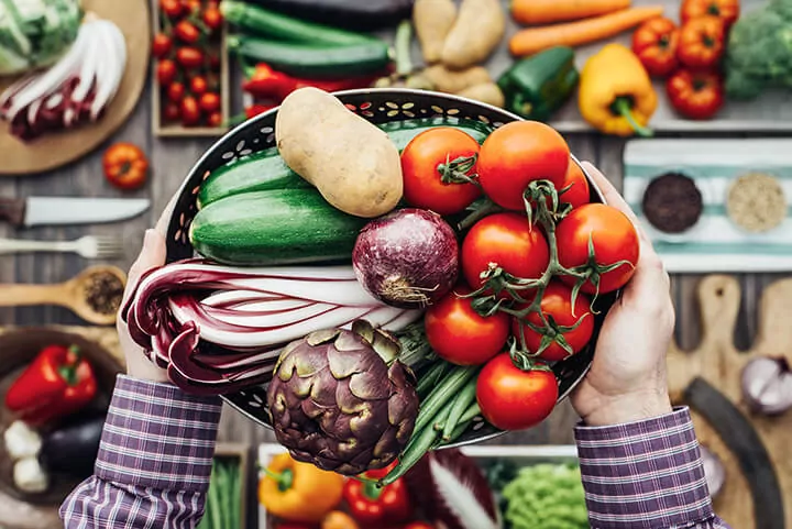 Man holding vegetables including tomatos, potato, cucumber, onion, green beans, and more