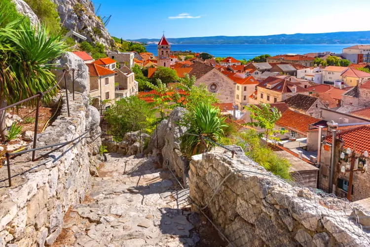 Sunny red roofs, Old city street with stone stairs and Church of St Michael in town and port Omis in Croatia