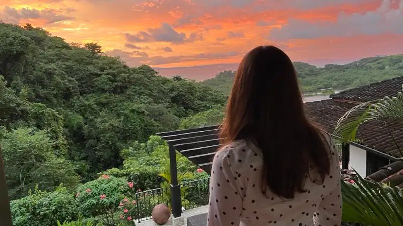 Kathleen Peddicord looks out over a lush, green landscape at sunset from a terrace with a pergola.