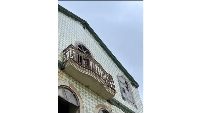 Close-up of an old tiled facade with arched windows and a rusted decorative balcony.