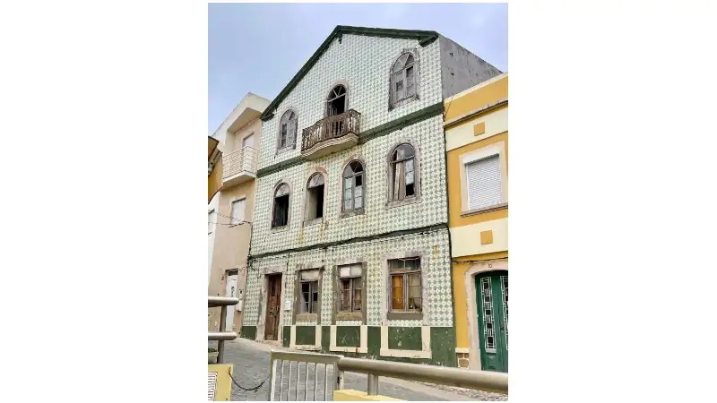 Old tiled building with arched windows and a small balcony, showing signs of wear and age.