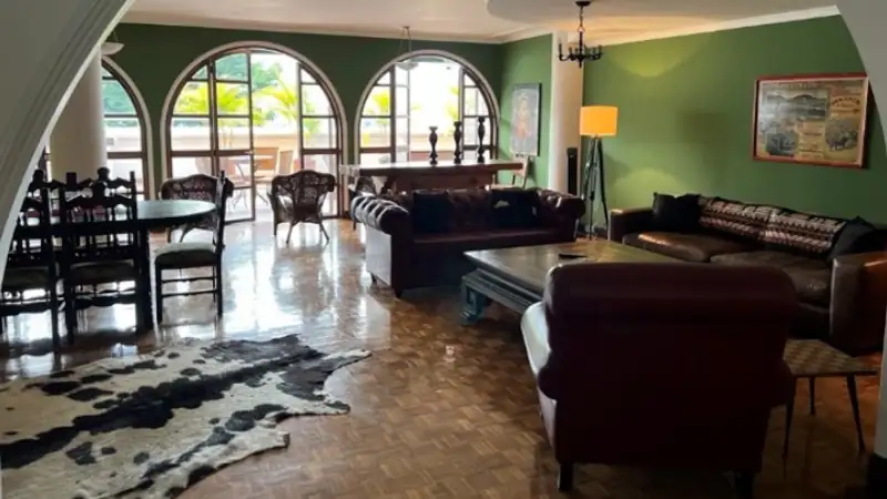 Bright, open living room with green walls, arched windows, leather seating, and polished wood floors, opening onto a sunlit terrace.