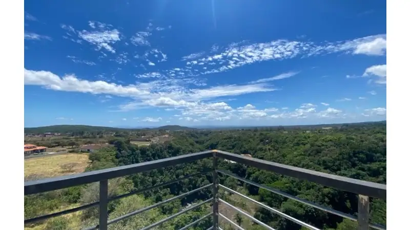 Enjoy breathtaking panoramic views from a modern balcony overlooking lush greenery, rolling hills, and a vibrant blue sky. A peaceful setting perfect for relaxation and nature lovers.