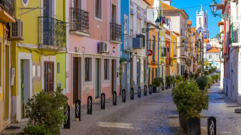 olorful old houses in a European street, narrow with its ancient buildings, European city. A cityscape of Setúbal with a white church in the distance.