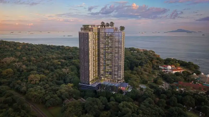 Modern luxury residential tower nestled in lush tropical forest along the coastline, offering panoramic ocean views and premium amenities.