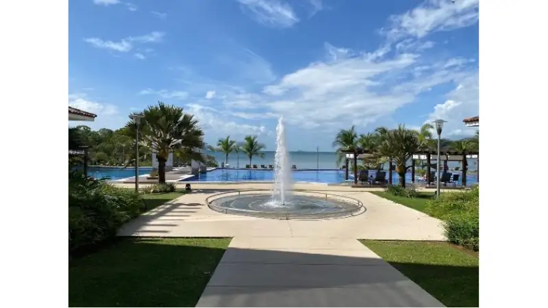 Manicured walkways lead to a central fountain, infinity pool, and stunning ocean views surrounded by tropical landscaping.