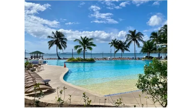 A stunning oceanfront swimming pool at The Westin Playa Bonita, featuring palm trees, sun loungers, crystal-clear turquoise water, and panoramic Pacific Ocean views.